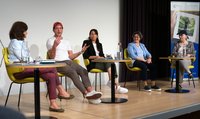 Fünf Personen sitzen verteilt an drei Tischen auf einer Bühne.