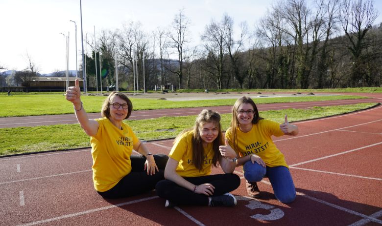 FRAGILE Spendenlauf Drei Frauen mit gelben T-Shirts sitzen auf der Laufbahn.