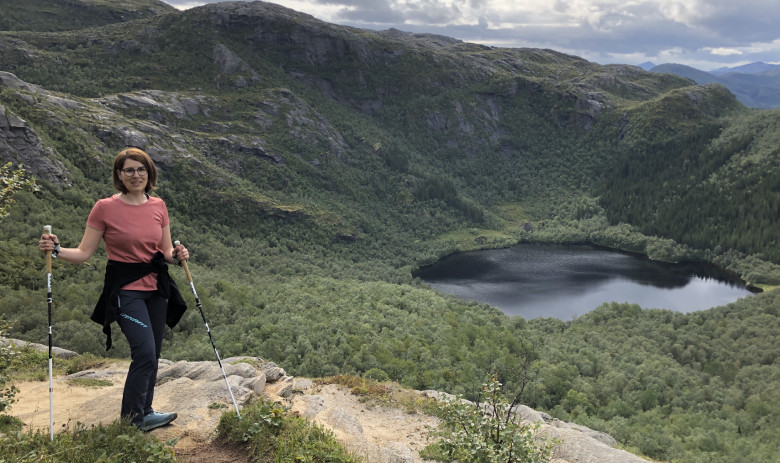 Eine Person mit Wanderstock steht in der nähe eines Berghangs. Ein wunderbarer Blick auf einen Bergsee im Hintergrund